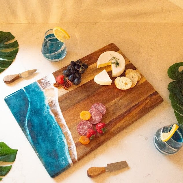 Wooden cutting board with assorted fruits, cheeses, and meats on a light wooden surface.