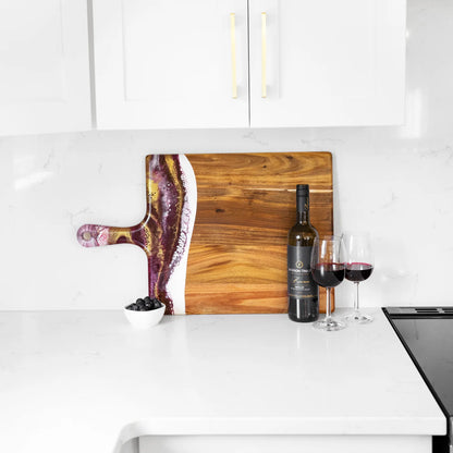 Wooden cutting board with a decorative edge on a kitchen counter with wine bottle and glasses.